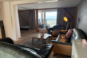 A modern living room with a sofa, a coffee table, and a lamp. There is a view of the outdoors through large windows. - Holiday apartment in Waren with swimming pool (Waren)