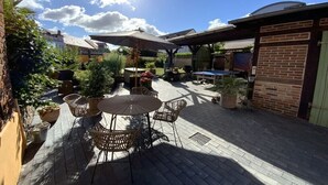 Eine Terrasse im Freien mit einem runden Tisch und Stühlen, umgeben von Blumentöpfen und einer Backsteinmauer.