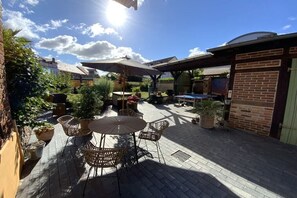 Eine Terrasse im Freien mit einem runden Tisch und Stühlen, umgeben von Blumentöpfen und einer Backsteinmauer.