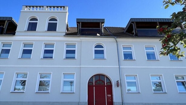 Ein mehrgeschossiges Gebäude mit roter Tür und weißen Fensterrahmen.