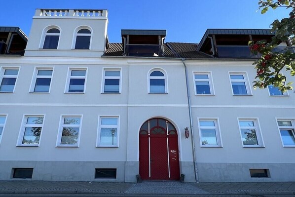 Ein mehrgeschossiges Gebäude mit roter Tür und weißen Fensterrahmen.