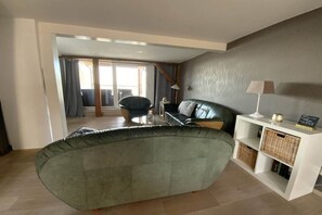 A living room with a green sofa, a white console table with baskets, and a view through a glass door to an outdoor area. - Holiday apartment in Waren with swimming pool (Waren)