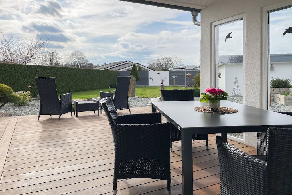 Un patio exterior con mesa y sillas, un seto y vistas de la propiedad.