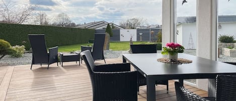 Un patio exterior con mesa y sillas, un seto y vistas de la propiedad.