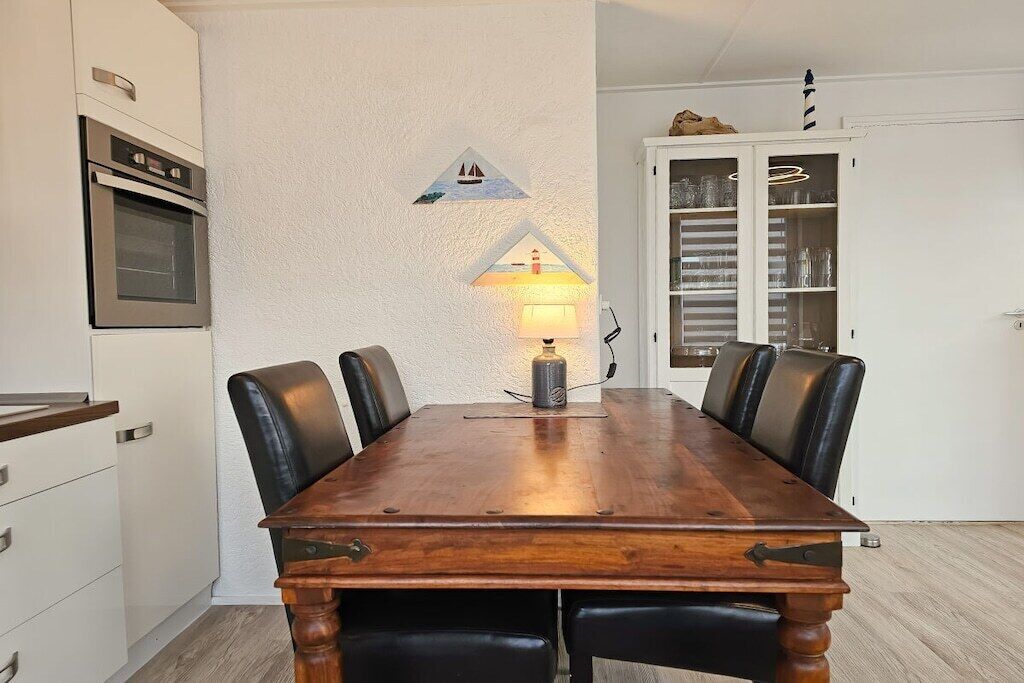 Ein Esstisch mit Stühlen, eine Wandlampe und ein Schrank mit Gläsern.