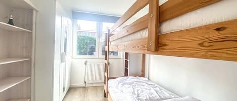 A bunk bed room with a window, white walls, and a radiator.