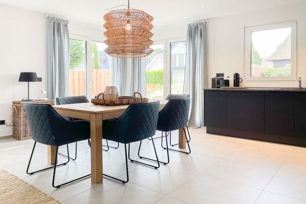 A modern kitchen with a dining area, featuring a large window, a black countertop, and a hanging light fixture.