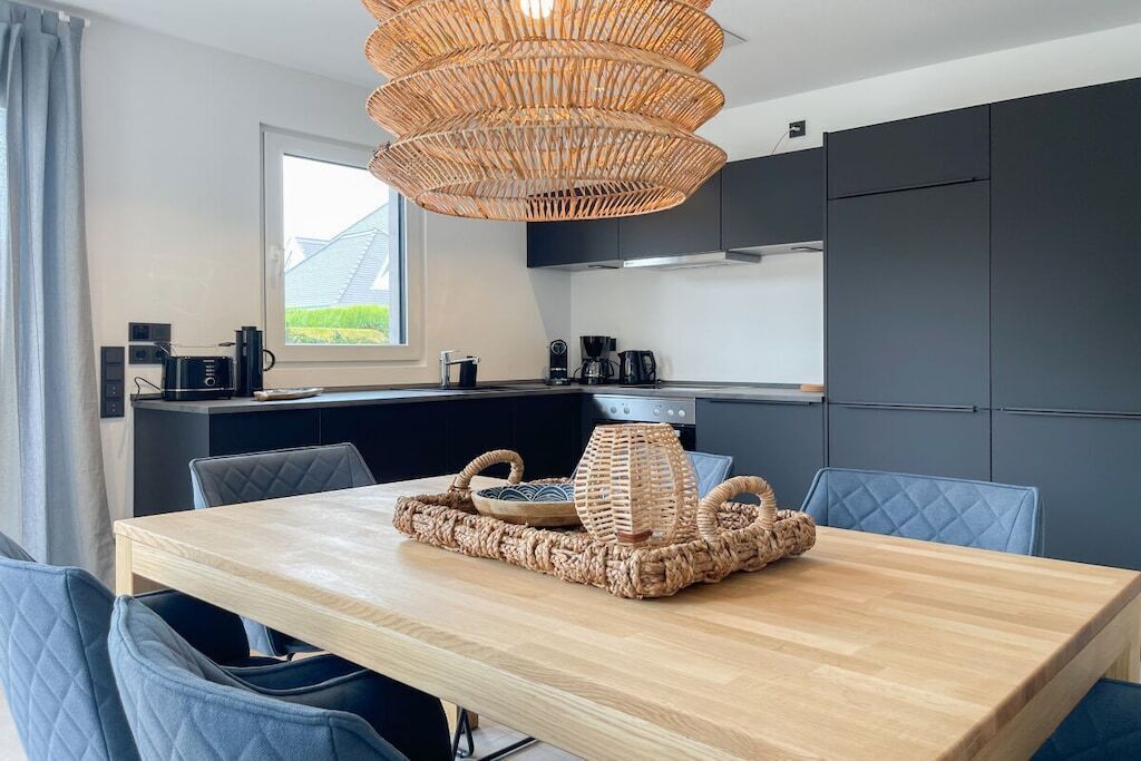 A modern kitchen with dark cabinetry, a wooden dining table with blue chairs, and a woven centerpiece.