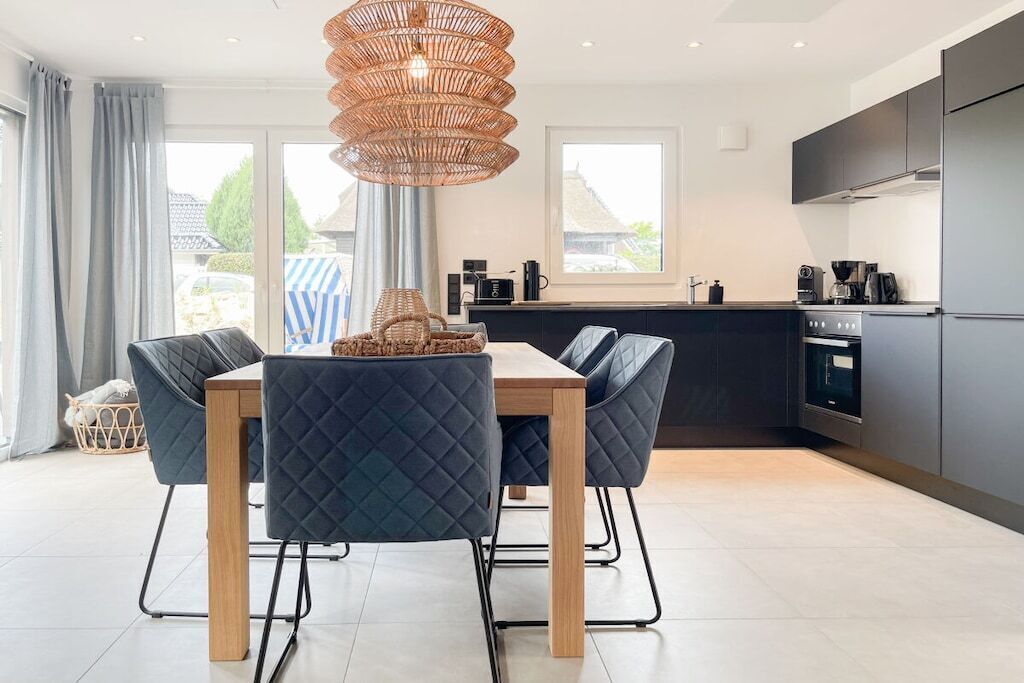 A modern kitchen with a dining area, featuring a large window, a hanging light fixture, and a built-in oven.