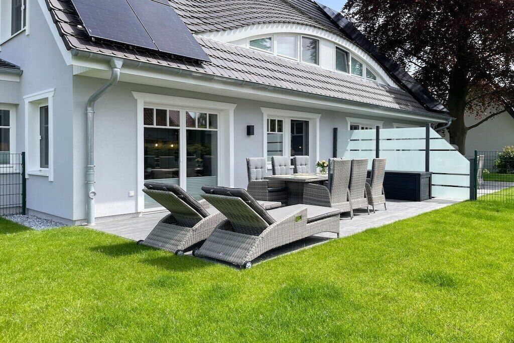 Ein Haus mit überdachter Terrasse, Gartenmöbeln und einer Solaranlage auf dem Dach.