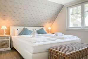 A bedroom with a large bed, two bedside lamps, a wicker bench, and a window with a view. - Holiday home with 4 bedrooms (Timmendorfer Strand)