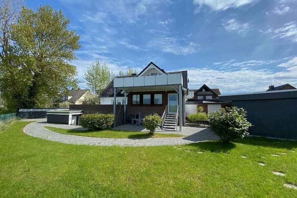 Ein modernes Haus mit überdachter Terrasse, einem kleinen Garten und blauem Himmel.