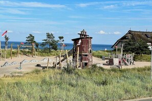 A beachside location with a wooden structure, a thatched-roof building, and a sandy area with flags. - Holiday apartment in Dahme with swimming pool (Dahme)