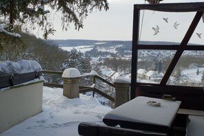 Ein mit Schnee bedeckter Balkon mit Blick auf eine Stadt und einem Holzbau mit einem Fenster.