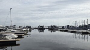 A marina with boats docked, calm water, and a cloudy sky.