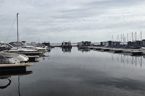 A marina with boats docked, calm water, and a cloudy sky.