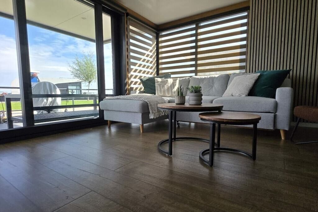 Ein modernes Wohnzimmer mit einem grauen Sofa, einem runden Couchtisch und Blick durch große Fenster.