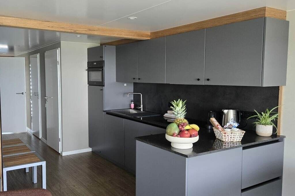 A modern kitchen with grey cabinets, a black countertop, and a fruit bowl.