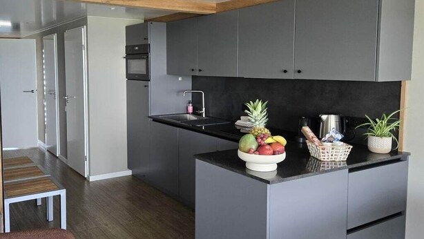 A modern kitchen with grey cabinets, a black countertop, and a fruit bowl.