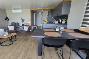 A modern dining area with a long table, black chairs, and a kitchen in the background.