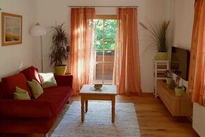 A cozy living room with a red sofa, a wooden coffee table, and a television on a wooden stand. - Villa in the woods - Eagle's nest (Roßhaupten)
