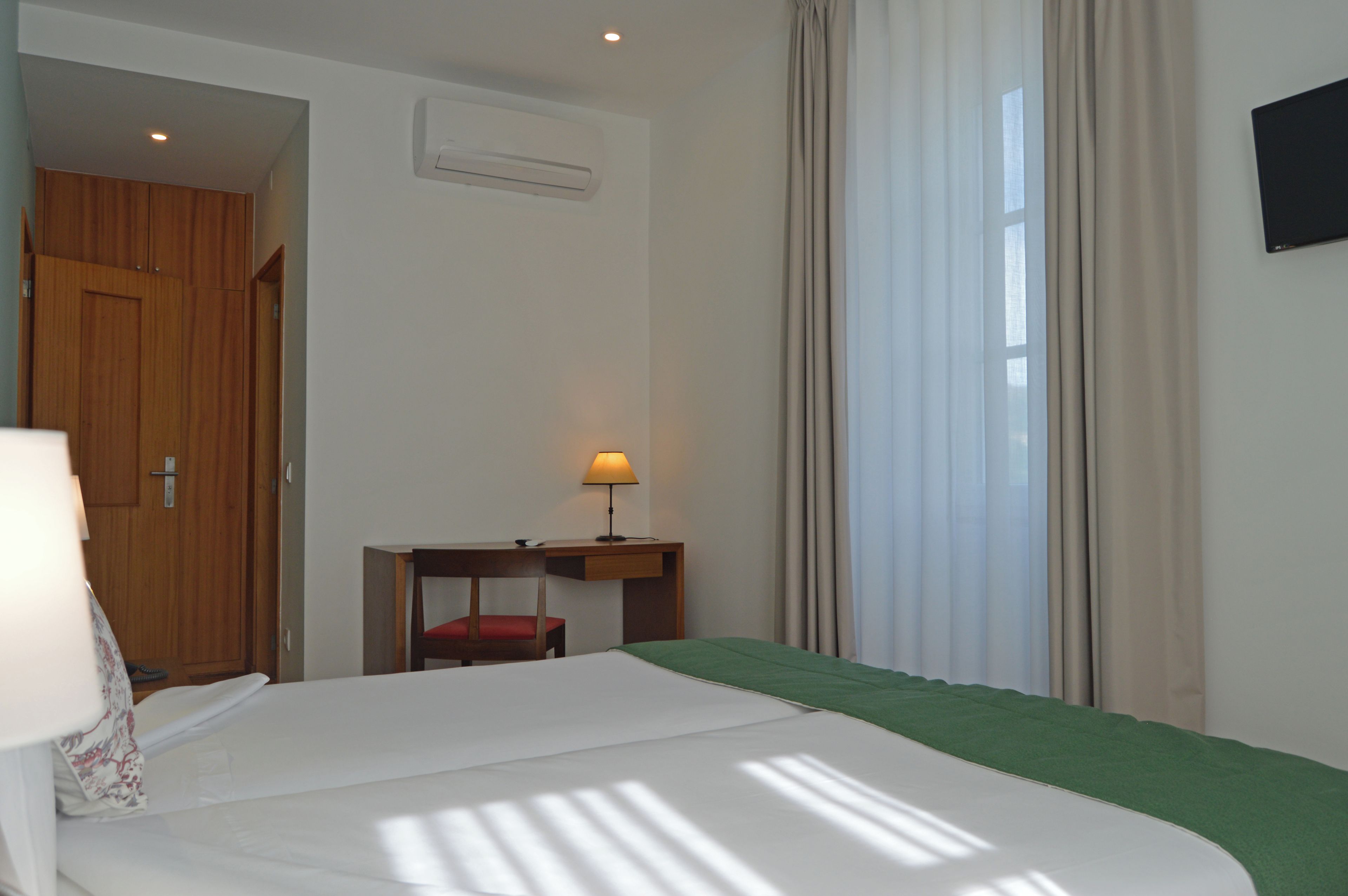 Habitación de hotel con cama, escritorio, silla, equipo de aire acondicionado y ventana con cortinas.