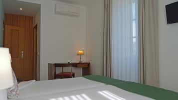 Habitación de hotel con cama, escritorio, silla, equipo de aire acondicionado y ventana con cortinas.