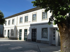 A white building with multiple windows and doors, a cobblestone street, and a tree in the foreground. - Casa São Bernardo de Claraval (Terras de Bouro)