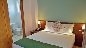 Habitación de hotel con cama, mesita de noche con lámpara, teléfono y almohada estampada.