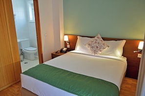 A hotel room with a bed, a bedside table with a lamp, a telephone, and a floral pillow. - Casa São Bernardo de Claraval (Terras de Bouro)
