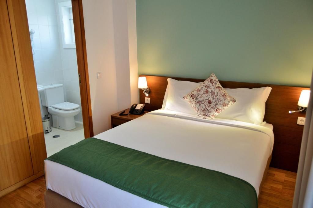Habitación de hotel con una cama, una mesita de noche con lámpara, un teléfono y un baño visible a través de una puerta abierta.