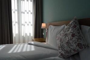 Habitación de hotel con cama, mesita de noche, lámpara y ventana con cortinas.
