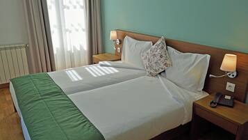 Ein Doppelbett mit grüner Bettdecke, zwei Nachttischlampen, ein Blumenkissen und ein Telefon auf einem Holznachttisch.
