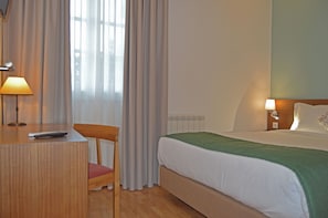 A hotel room with a bed, a desk with a lamp, a chair, and a window with curtains. - Casa São Bernardo de Claraval (Terras de Bouro)