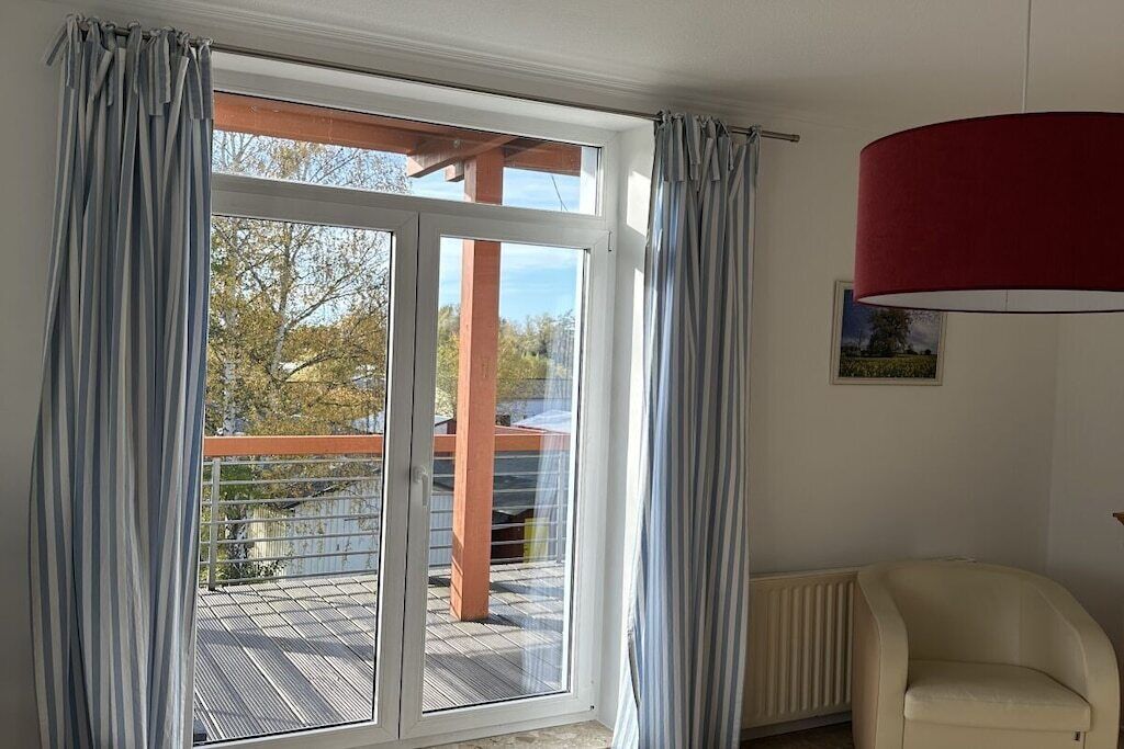 Una habitación con puerta de vidrio corredera que da a un balcón, un radiador y una silla.