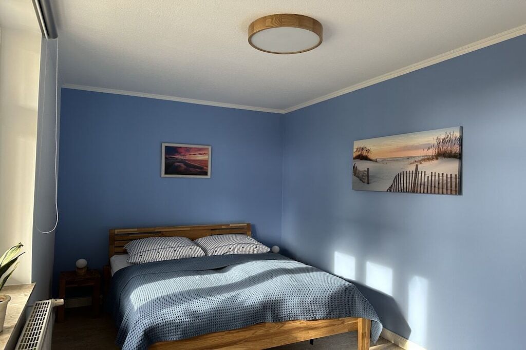 Une chambre à coucher comprenant un lit, une table de chevet, un tableau accroché au mur et un luminaire fixé au plafond.