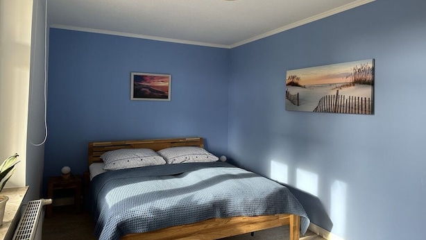 Ein Schlafzimmer mit einem Bett, einem Nachttisch, einem Wandbild und einer Deckenleuchte.