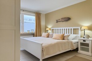 Een slaapkamer met een bed, nachtlampjes, een raam met gordijnen en een visdecoratie aan de muur.