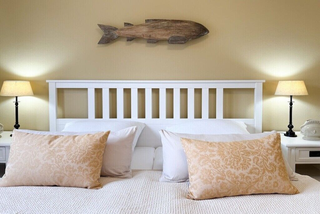 Un dormitorio con cabecera blanca, dos lámparas de noche y un cuadro decorativo con peces.