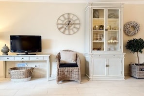 A living room with a television, wicker chair, white cabinet, and decorative items. - Holiday apartment with 1 bedroom (Timmendorfer Strand)