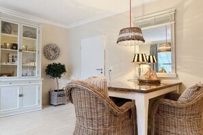 Een eethoek met rieten stoelen, een tafel en een hanglamp.