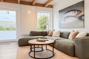 A modern living room with a sectional sofa, a round coffee table, and a large painting of a fish on the wall. - Holiday home with 3 bedrooms (Timmendorfer Strand\/Niendorf)
