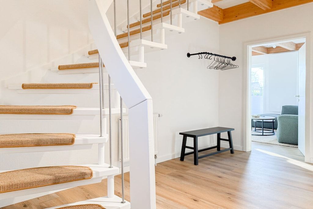 A modern interior with a staircase, a bench, and a hanging clothes rack.