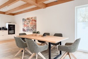 A modern kitchen with a wooden table and chairs, a painting on the wall, and a window with blinds. - Holiday home with 3 bedrooms (Timmendorfer Strand\/Niendorf)