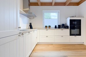 A modern kitchen with white cabinetry, a microwave, and a window with blinds. - Holiday home with 3 bedrooms (Timmendorfer Strand\/Niendorf)