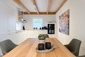 A modern kitchen with white cabinetry, a wooden dining table, and a large abstract painting on the wall. - Holiday home with 3 bedrooms (Timmendorfer Strand\/Niendorf)