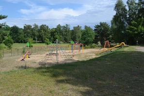 A playground with various play structures, including a climbing net, swings, and a slide. - Holiday home in Userin with swimming pool (Userin)