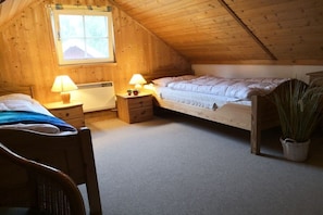 A cozy attic bedroom with two beds, wooden walls, a window, and a chair. - Holiday home in Userin with swimming pool (Userin)