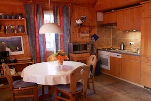 A wooden interior with a round dining table, chairs, a kitchen area with appliances, and a colorful curtain. - Holiday home in Userin with swimming pool (Userin)