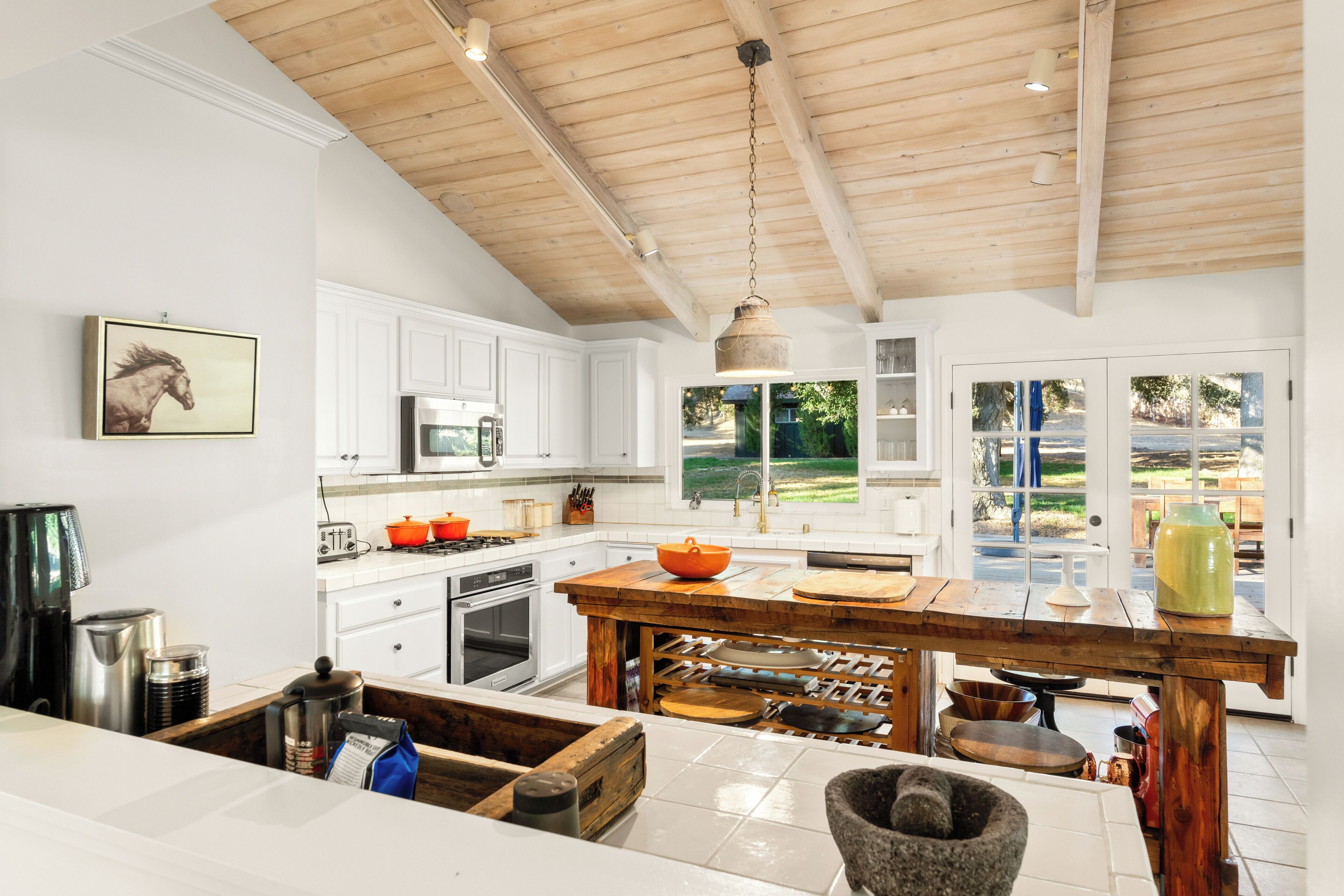 A modern kitchen with white cabinetry, a wooden ceiling, and a large island with various kitchen tools.